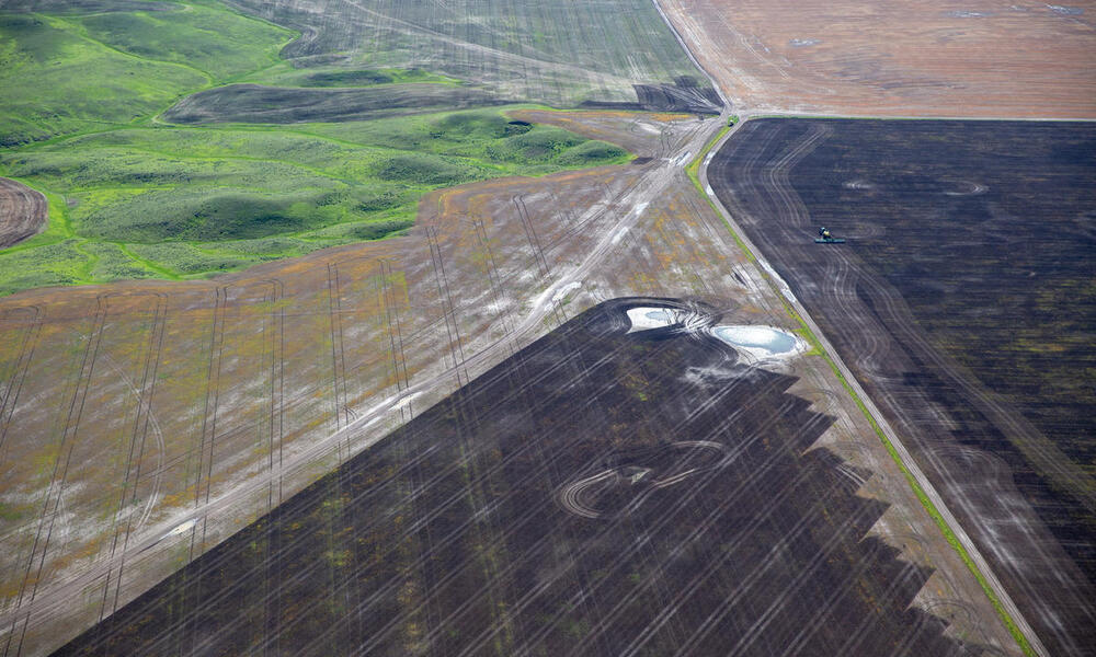 A patchwork of plowed brown land next to some remaining intact green grasslands