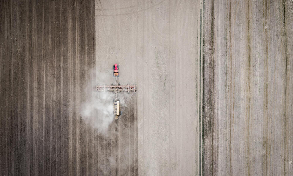 An aerial view of a red tractor plowing up grassland