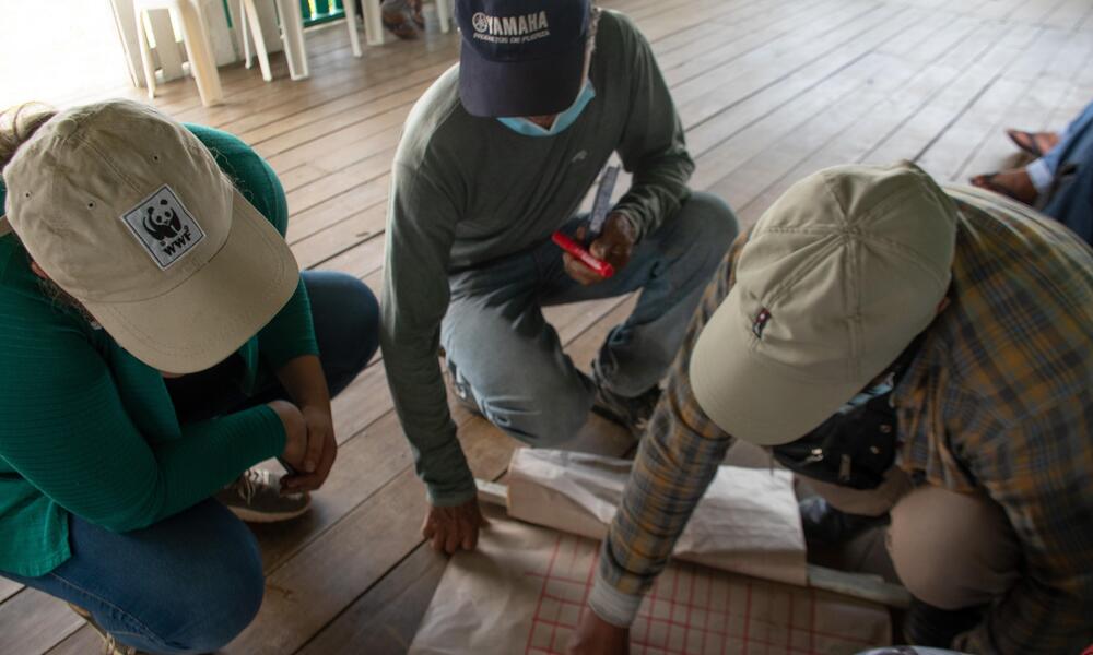 Three people hover over a document as they discuss livestock production and regenerative ranching in Madre de Dios region of Peruvian Amazon