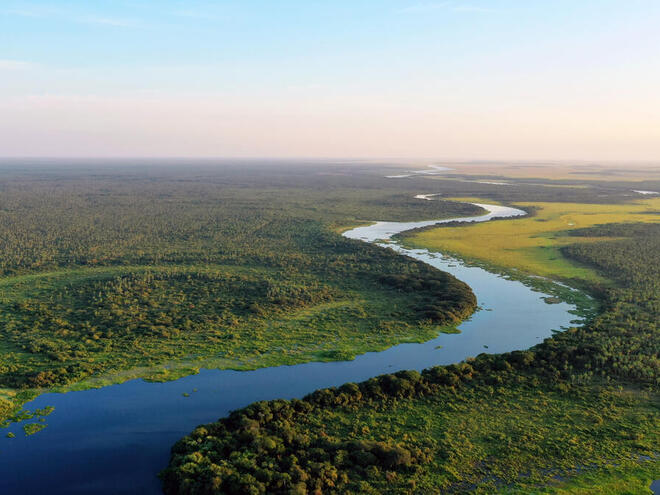 Aerial view of a blue river snaking through green lands