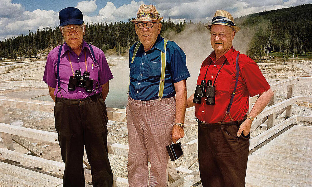 Three men pose for a photo in front of geysers