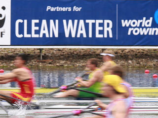 Blurred rowers with clean water sign in the background.