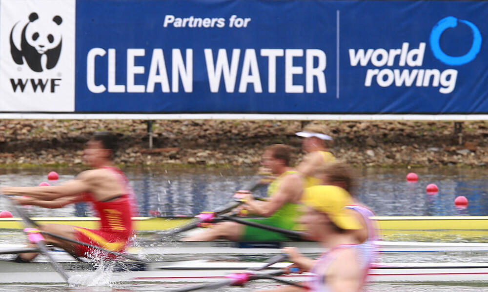 Blurred rowers with clean water sign in the background.