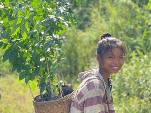 Young girl carrying seedling on her back and smiling in Laos